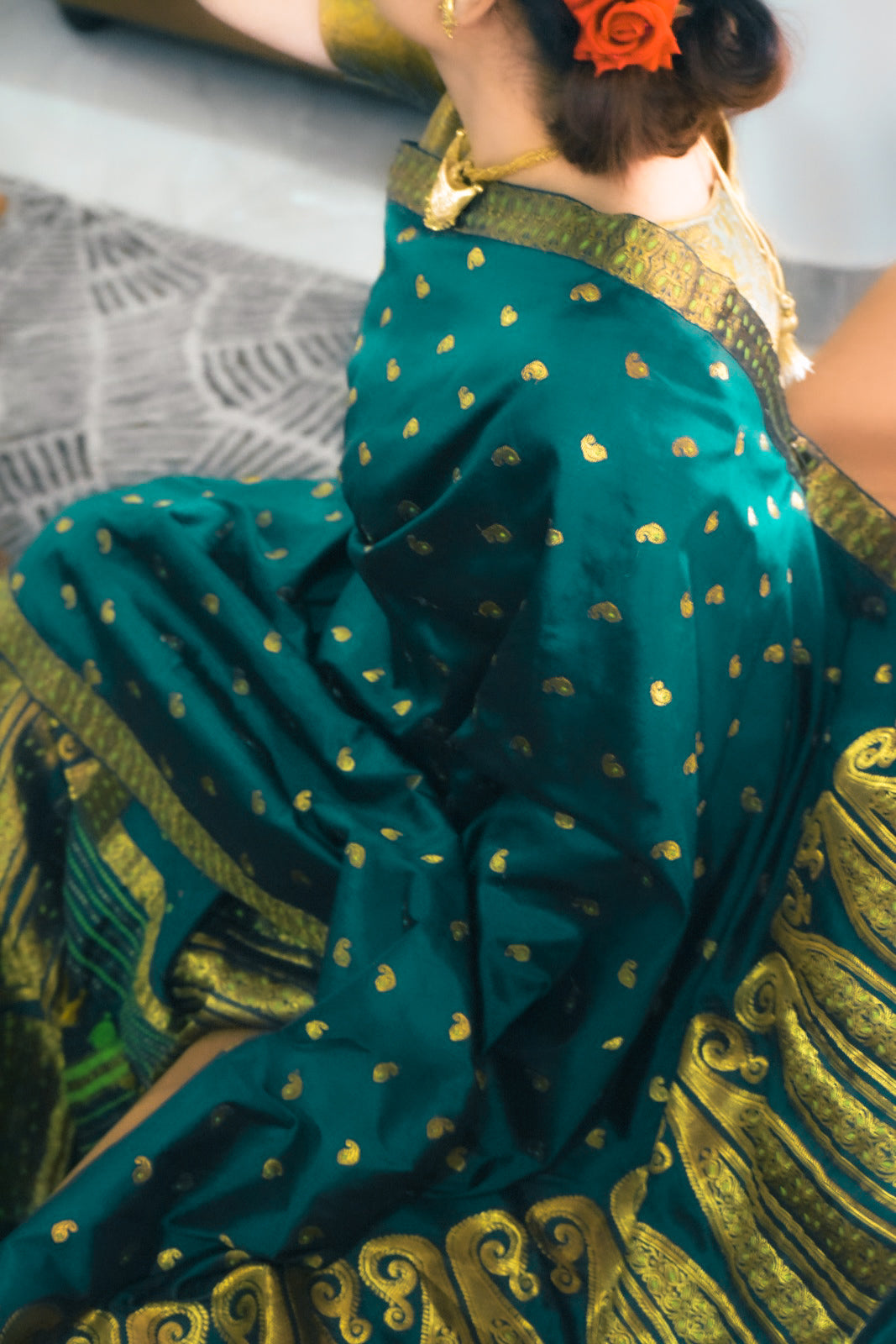 Green saree with gold patterns worn by a person, sitting on a textured surface.